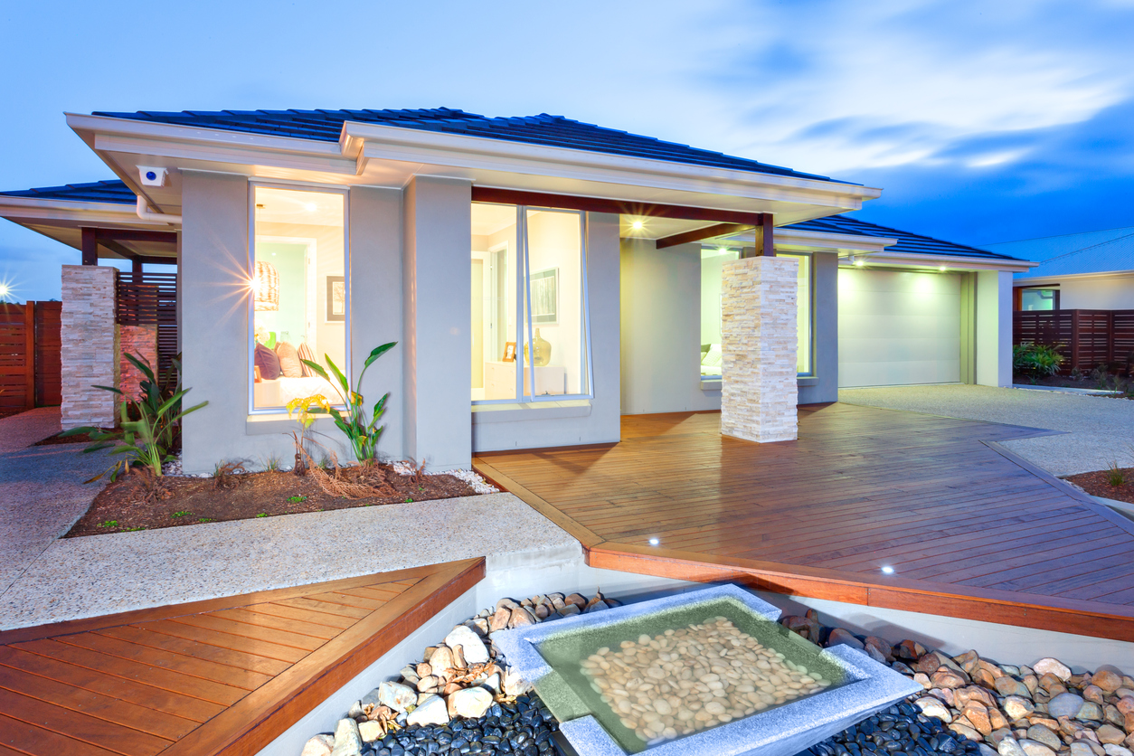 This luxury house has lights on inside and outside due to the darkened environment. there are lights even on the wooden floor of the facade. The garden filled from stones with small water pond and concrete yard cover by the light of the house